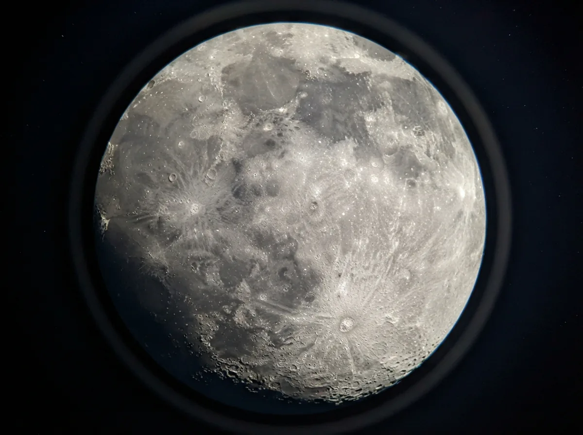 A view through the telescope eyepiece showing a bright, detailed image of the Moon's craters and surface.